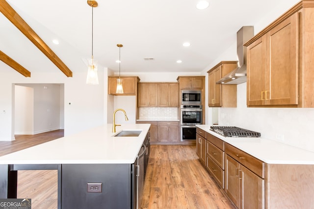 kitchen with beam ceiling, sink, stainless steel appliances, an island with sink, and light wood-type flooring