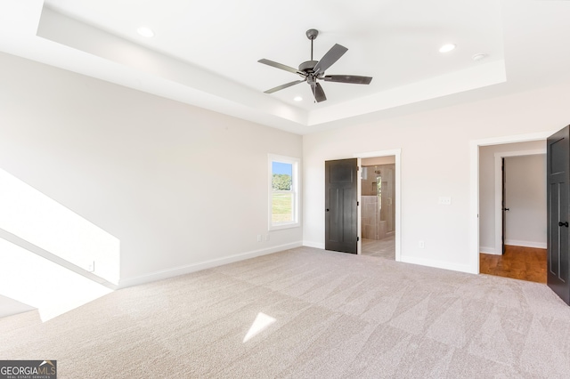 unfurnished bedroom with light carpet, connected bathroom, a raised ceiling, and ceiling fan