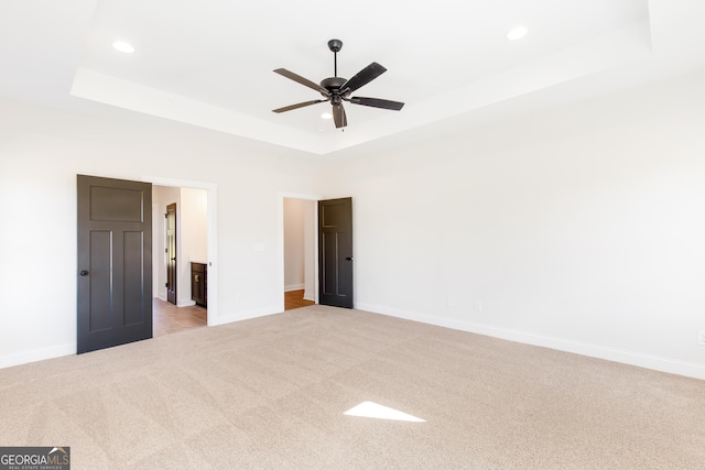 carpeted empty room with ceiling fan and a raised ceiling