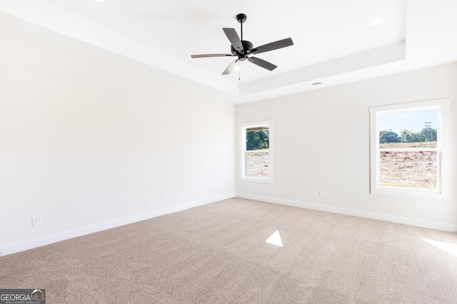 empty room with ceiling fan, carpet floors, and a tray ceiling