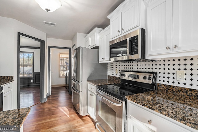 kitchen with dark stone counters, dark hardwood / wood-style floors, appliances with stainless steel finishes, tasteful backsplash, and white cabinetry