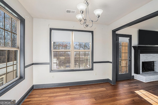 unfurnished dining area with a fireplace, a chandelier, and dark hardwood / wood-style floors