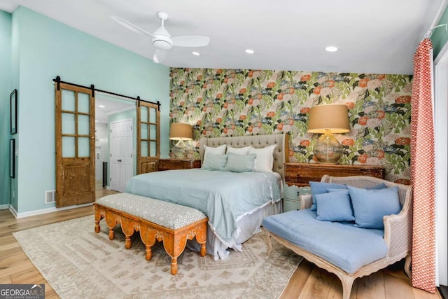 bedroom featuring a closet, a barn door, light hardwood / wood-style floors, and ceiling fan