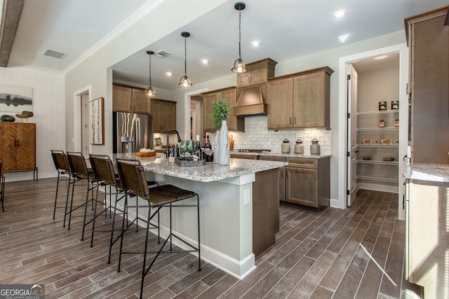 kitchen featuring a kitchen bar, stainless steel appliances, dark wood-type flooring, pendant lighting, and an island with sink