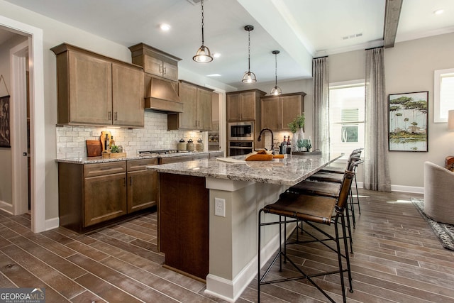 kitchen featuring pendant lighting, premium range hood, dark wood-type flooring, light stone countertops, and appliances with stainless steel finishes