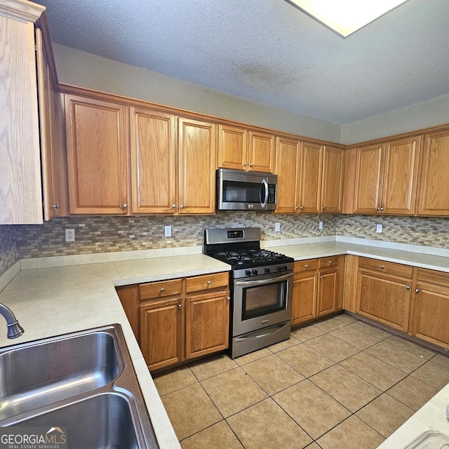 kitchen with backsplash, a textured ceiling, stainless steel appliances, sink, and light tile patterned flooring