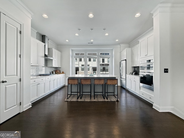 kitchen with a breakfast bar, stainless steel appliances, dark wood-type flooring, white cabinetry, and an island with sink