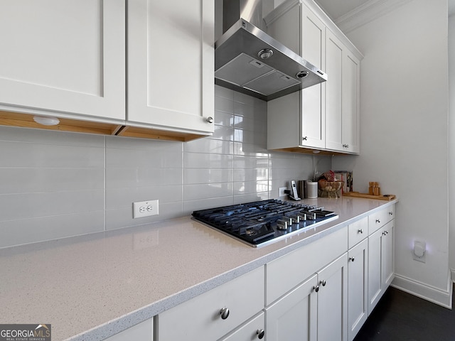 kitchen with decorative backsplash, ornamental molding, wall chimney range hood, white cabinetry, and stainless steel gas stovetop