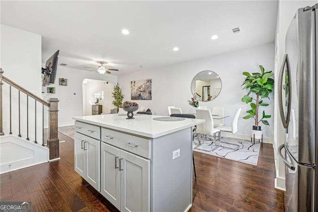 kitchen featuring stainless steel fridge, dark hardwood / wood-style flooring, a breakfast bar, ceiling fan, and a center island