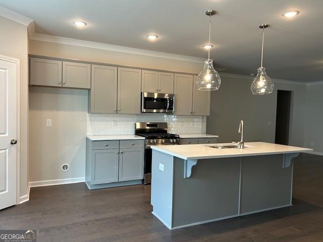 kitchen featuring a center island with sink, sink, dark hardwood / wood-style floors, appliances with stainless steel finishes, and decorative light fixtures