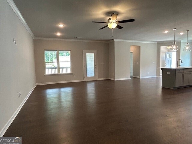 unfurnished living room featuring ornamental molding, ceiling fan with notable chandelier, dark wood-type flooring, and sink