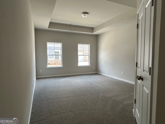 empty room featuring a raised ceiling and dark colored carpet