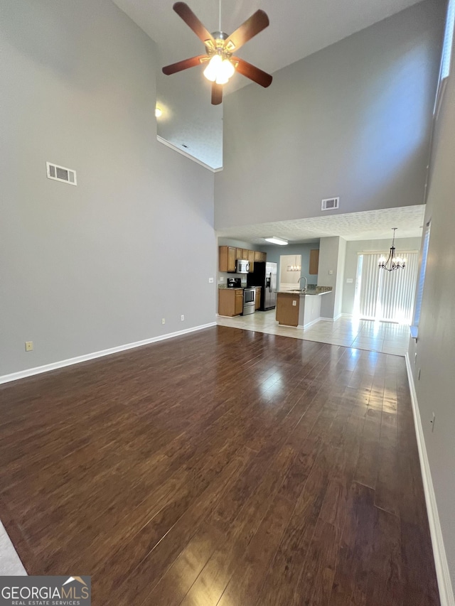 unfurnished living room featuring high vaulted ceiling, dark wood-type flooring, and ceiling fan with notable chandelier