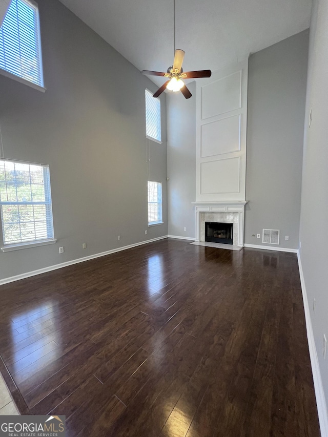 unfurnished living room featuring a towering ceiling, dark hardwood / wood-style floors, a wealth of natural light, and ceiling fan