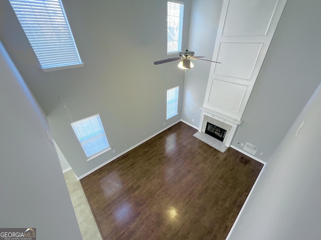 unfurnished living room with ceiling fan, a towering ceiling, and dark wood-type flooring