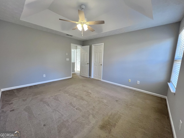 empty room with ceiling fan, carpet floors, and a tray ceiling