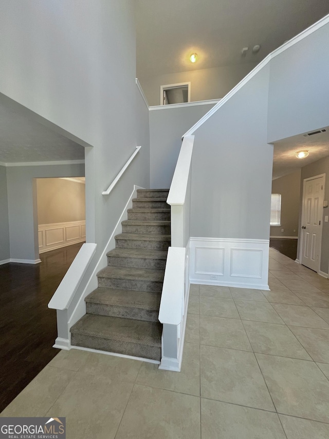 staircase featuring tile patterned floors, a towering ceiling, and ornamental molding