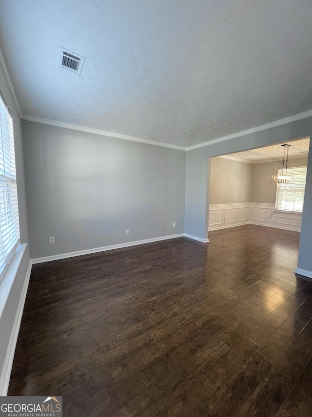 spare room with a textured ceiling, dark hardwood / wood-style floors, an inviting chandelier, and crown molding