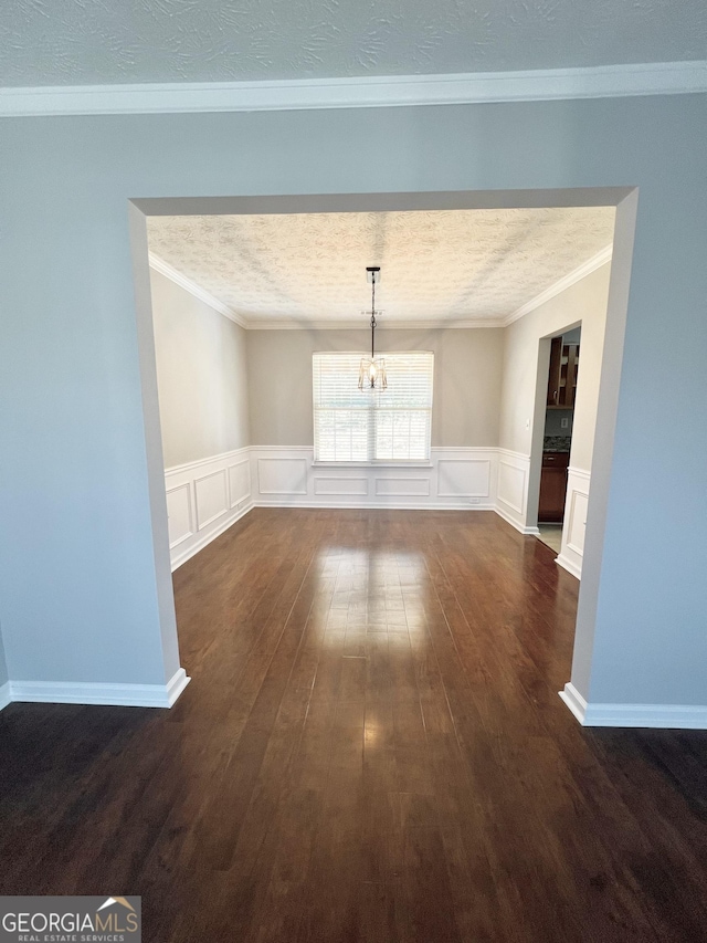 unfurnished dining area featuring dark hardwood / wood-style flooring, ornamental molding, a textured ceiling, and a chandelier