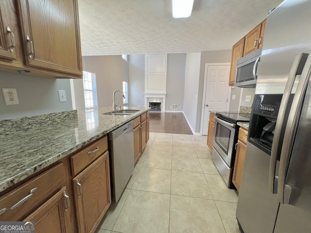 kitchen with light stone countertops, appliances with stainless steel finishes, a textured ceiling, sink, and light tile patterned flooring