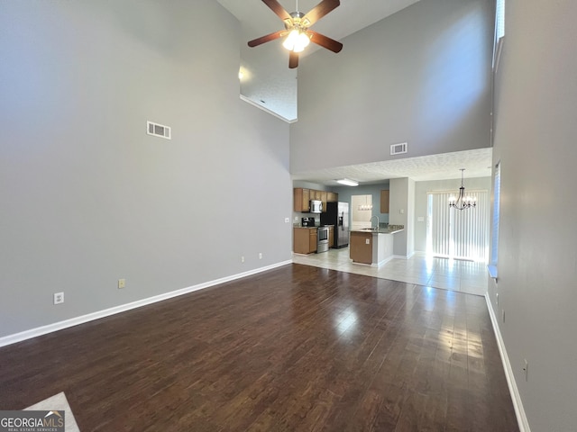 unfurnished living room with sink, a towering ceiling, dark wood-type flooring, and ceiling fan with notable chandelier