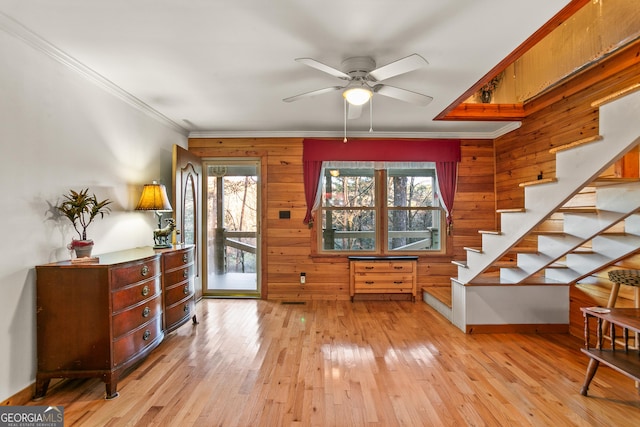 interior space with ceiling fan, light hardwood / wood-style floors, ornamental molding, and wooden walls