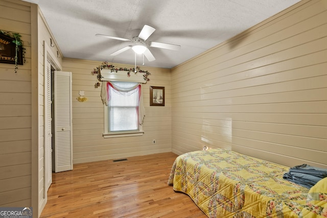 bedroom with ceiling fan, light wood-type flooring, a textured ceiling, and wooden walls