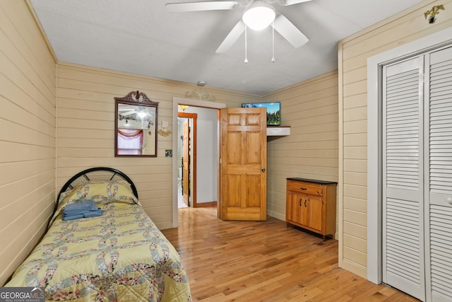 bedroom featuring light wood-type flooring, a closet, ceiling fan, and wood walls