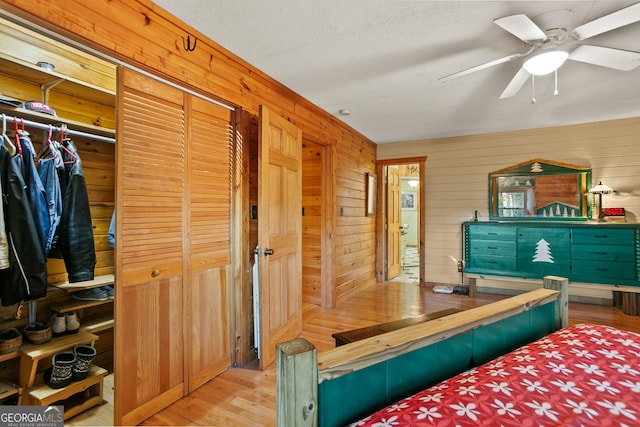 bedroom with ceiling fan, a closet, wood walls, and light wood-type flooring