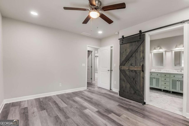 unfurnished bedroom featuring a barn door, light hardwood / wood-style floors, ensuite bath, and ceiling fan