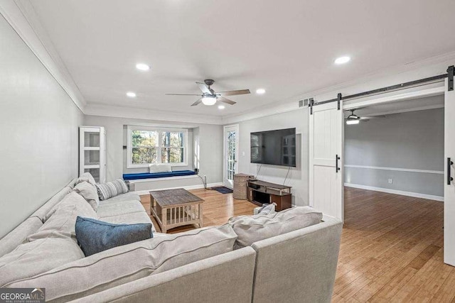 living room with wood-type flooring, a barn door, ceiling fan, and ornamental molding