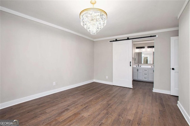 unfurnished bedroom with a barn door, ensuite bath, dark hardwood / wood-style floors, and ornamental molding