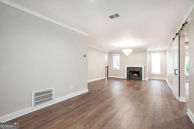 unfurnished living room with a barn door, dark hardwood / wood-style floors, an inviting chandelier, and ornamental molding