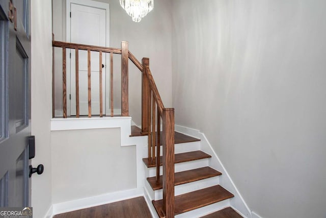 staircase with hardwood / wood-style floors and a notable chandelier