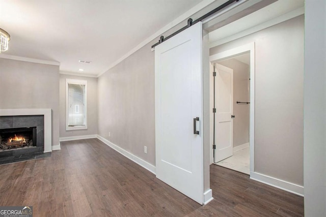 unfurnished living room featuring a fireplace, a barn door, dark hardwood / wood-style floors, and ornamental molding