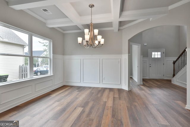 unfurnished dining area featuring an inviting chandelier, beam ceiling, dark hardwood / wood-style floors, coffered ceiling, and ornamental molding