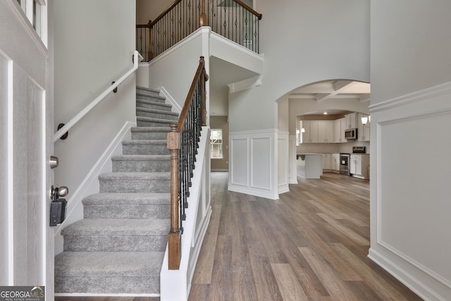 stairs featuring hardwood / wood-style flooring, coffered ceiling, a towering ceiling, and beam ceiling