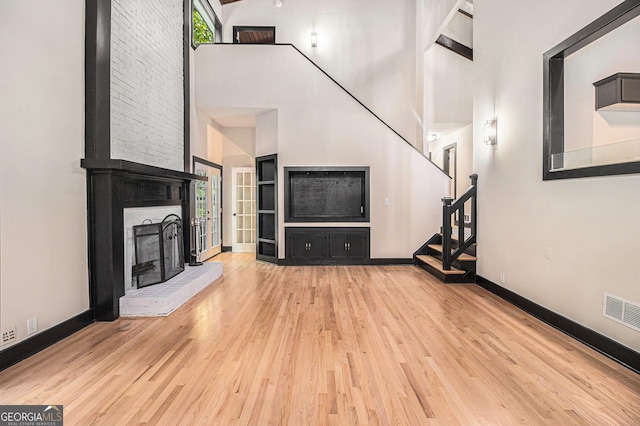 unfurnished living room featuring a fireplace, high vaulted ceiling, and light hardwood / wood-style flooring