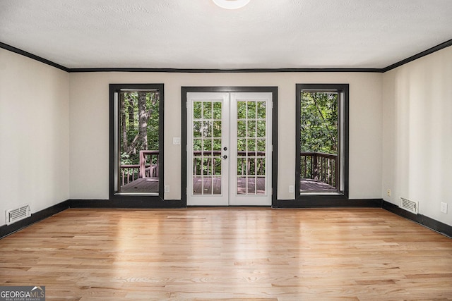 empty room featuring french doors, light hardwood / wood-style flooring, a textured ceiling, and ornamental molding