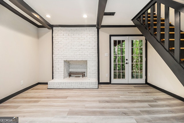 unfurnished living room with french doors, crown molding, a fireplace, beam ceiling, and light hardwood / wood-style floors