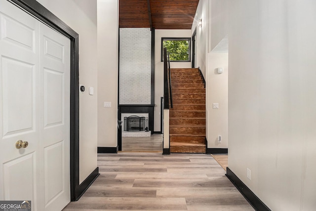 corridor with light wood-type flooring, lofted ceiling, and wood ceiling