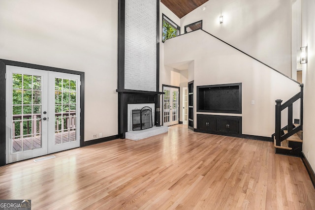 unfurnished living room with a brick fireplace, light wood-type flooring, high vaulted ceiling, and french doors