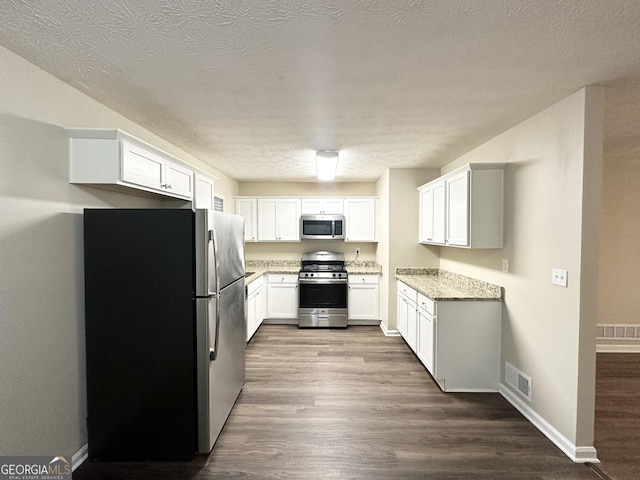 kitchen with dark hardwood / wood-style floors, light stone countertops, a textured ceiling, appliances with stainless steel finishes, and white cabinetry