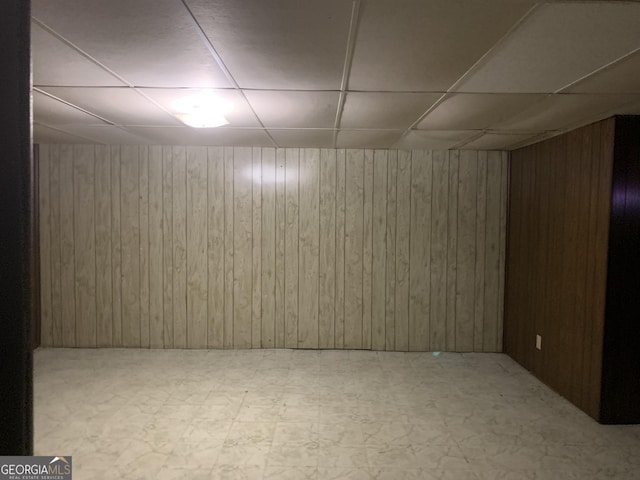 basement featuring a paneled ceiling and wood walls