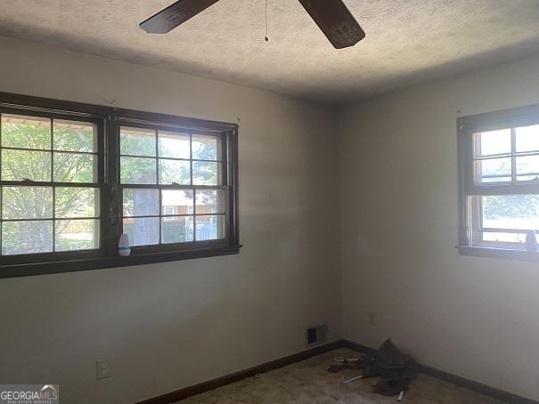 unfurnished room featuring a textured ceiling, ceiling fan, and a healthy amount of sunlight