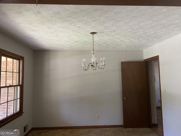 carpeted empty room featuring a chandelier and a textured ceiling