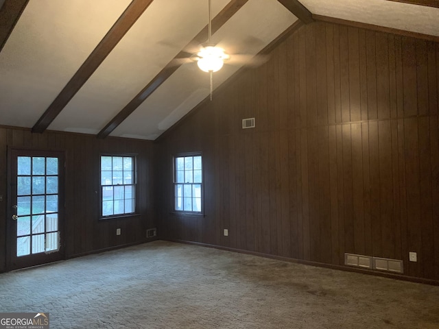 carpeted empty room featuring ceiling fan, lofted ceiling with beams, and wooden walls