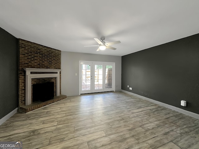 unfurnished living room featuring ceiling fan, light hardwood / wood-style flooring, french doors, and a brick fireplace