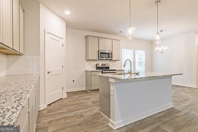 kitchen with gray cabinetry, decorative backsplash, light wood-type flooring, and appliances with stainless steel finishes