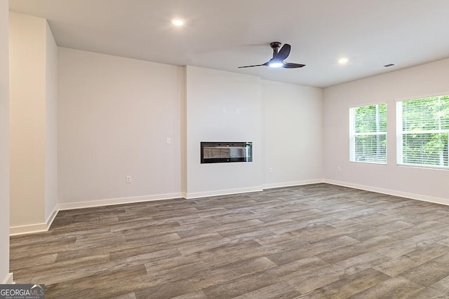 unfurnished living room featuring a glass covered fireplace, wood finished floors, visible vents, and baseboards